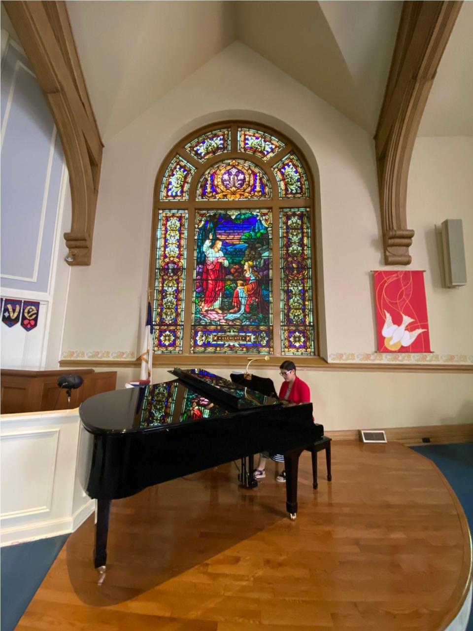 Pastor LydiaGrace Quine-Espiritu Gray plays piano near the Tiffany window inside the First Presbyterian Church sanctuary.