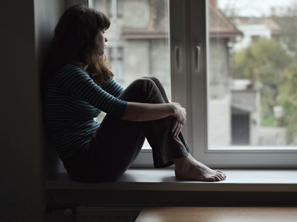 Sad young woman sitting on the window, watching out