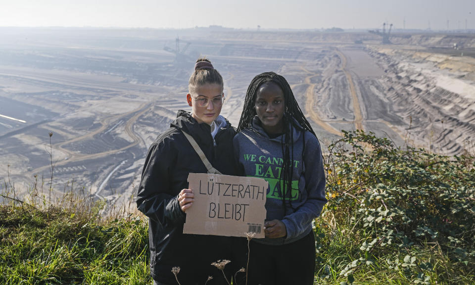 Climate activists Vanessa Nakate from Uganda, right, and Leonie Bremer of the German Fridays for Future movement, hold a sign that reads: "Luetzerath stays" during their visit to the Garzweiler open-cast coal mine in Luetzerath, western Germany, Saturday, Oct. 9, 2021. The village of Luetzerath, now almost entirely abandoned as the mine draws ever closer, will be the latest village to disappear as coal mining at the Garzweiler mine expands. Garzweiler, operated by utility giant RWE, has become a focus of protests by people who want Germany to stop extracting and burning coal as soon as possible. (AP Photo/Martin Meissner)