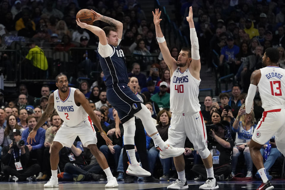 Dallas Mavericks guard Luka Doncic jumps to pass against Los Angeles Clippers defenders Ivica Zubac (40), Paul George (13) and Kawhi Leonard (2) during the first half of an NBA basketball game in Dallas, Sunday, Jan. 22, 2023. (AP Photo/LM Otero)