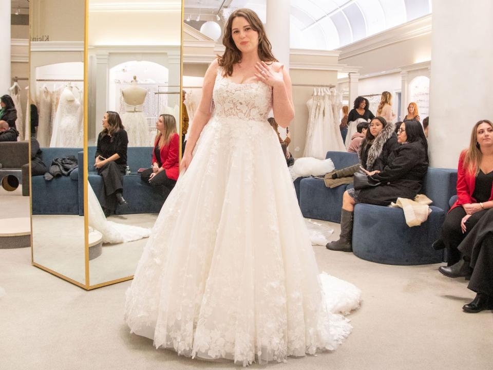 A woman stands in a wedding dress in a bridal boutique.