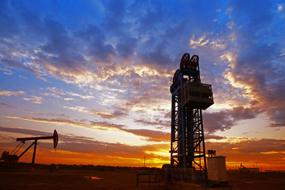 An oil pump and drilling rig at sunset