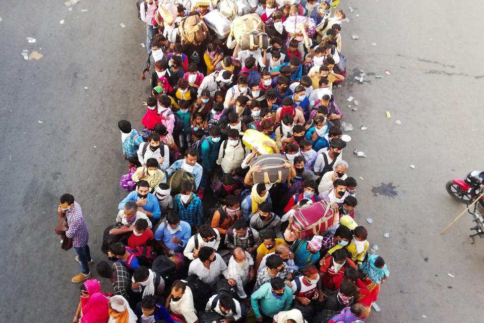 Migrant workers and their family members lineup outsdie the Anand Vihar bus terminal to leave for their villages during a government-imposed nationwide lockdown as a preventive measure against the COVID-19 coronavirus in New Delhi on March 28, 2020. - Tens of thousands of migrant workers and their famiies on March 28 fought and shoved their way onto buses organised by India's most populous state to get them to their home towns amid the coronavirus pandemic. (Photo by Bhuvan BAGGA / AFP) (Photo by BHUVAN BAGGA/AFP via Getty Images)