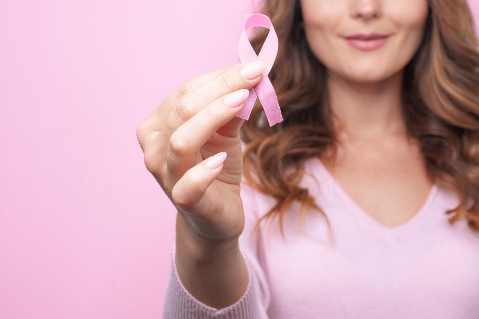 Woman in pink sweater with pink ribbon supporting breast cancer awareness campaign. Breast Cancer Awareness Month