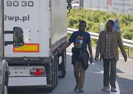 Migrants check the trailer of a truck during an attempt to make a clandestine crossing to England through the Channel tunnel as lorries wait on a road which leads to the Channel Tunnel terminal in Coquelles near Calais, northern France, July 1, 2015. REUTERS/Vincent Kessler