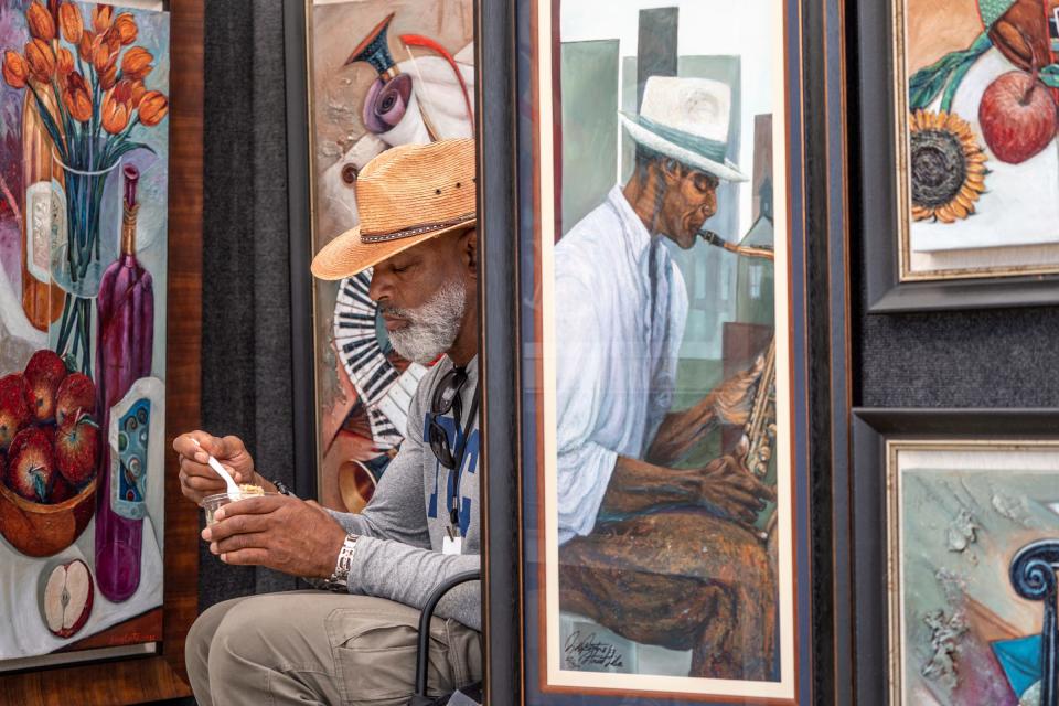 Artist Sidney Carter of Powder Springs, Ga., takes a lunch break among his acrylic paintings at his booth during Arts, Beats & Eats in Royal Oak on Friday, Sept. 1, 2023.