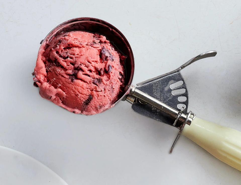 an ice cream scooper with a large scoop of homemade cherries jubilee ice cream