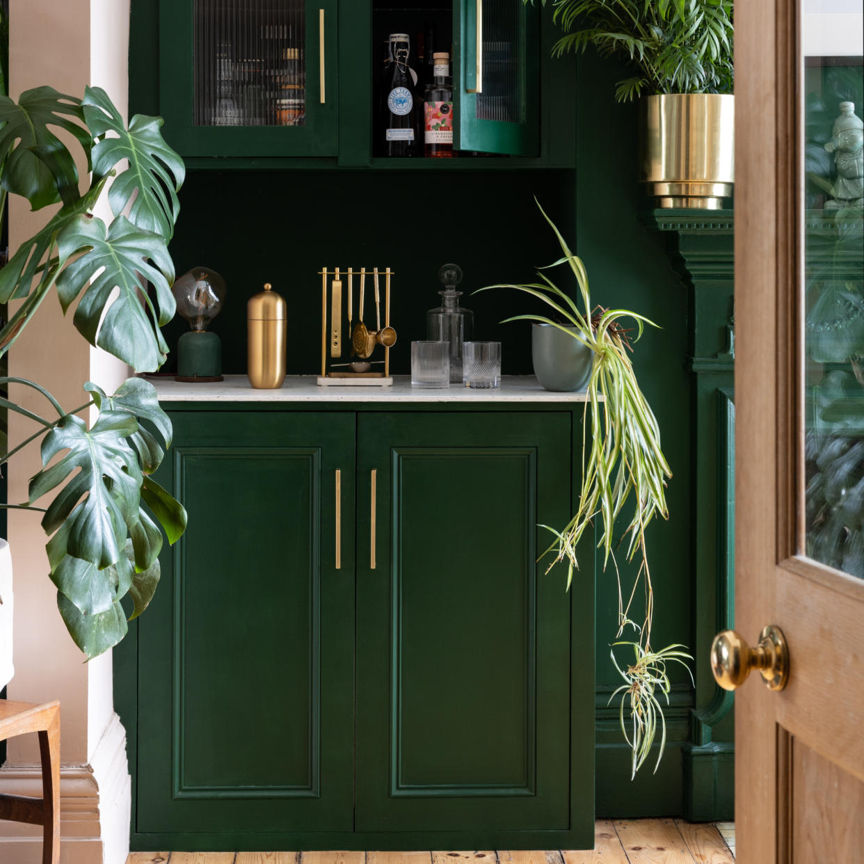  Green painted kitchen cabinets with brass handles and displayed houseplants. 