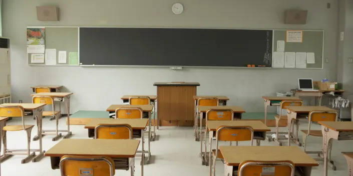 View of desks from the back of an empty classroom facing a chalkboard