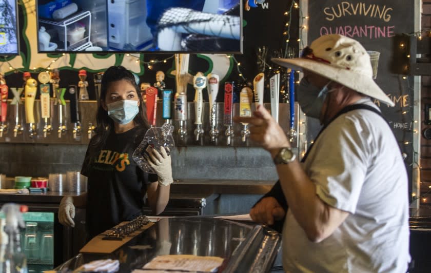 PLACENTIA, CA - MAY 16: Bartender Brianna Van De Mortel takes a beer order from a customer at Kelly's Korner on Saturday, May 16, 2020 in Placentia, CA. The sports bar is effectively grounded as the pandemic shutdowns affecting all restaurants limit them to take-out. Like most restaurants and bars, Kelly's has had to pivot drastically to survive. (Brian van der Brug / Los Angeles Times)