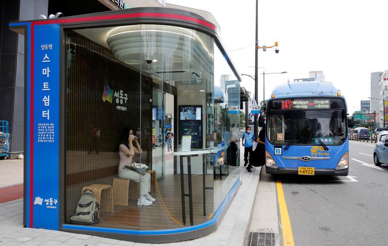 Woman waits for a bus inside a glass-covered bus stop in Seoul