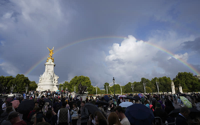 People gather outside Buckingham Palace in London as a double rainbow appears in the sky