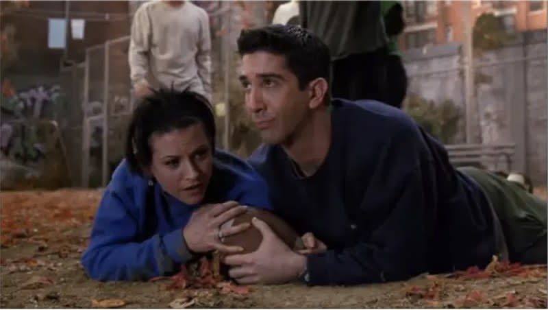 Monica and Ross lying on the ground and holding a football