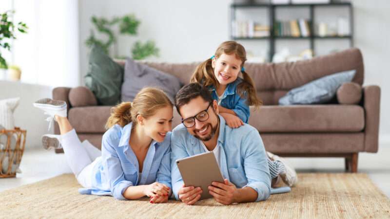 A father, mother, and little girl happily look at a tablet.