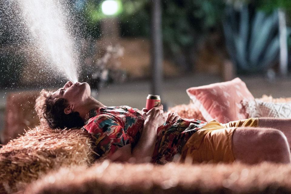 Nyles lying on a stack of hay and spraying his drink into the air