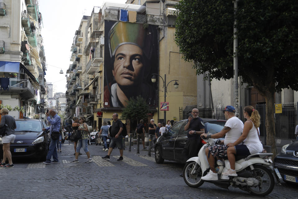 People walk past a giant mural of city patron Saint San Gennaro in downtown Naples, Italy, Wednesday, Sept. 18, 2019. The way the local Catholic church is intertwined with Napoli only heightens the feeling that following the team is a religion. (AP Photo/Gregorio Borgia)