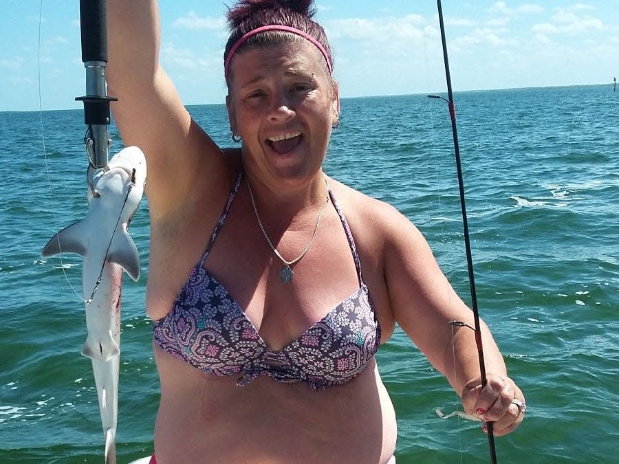 A woman on a boat in a bikini holding up a fish and a fishing rod.