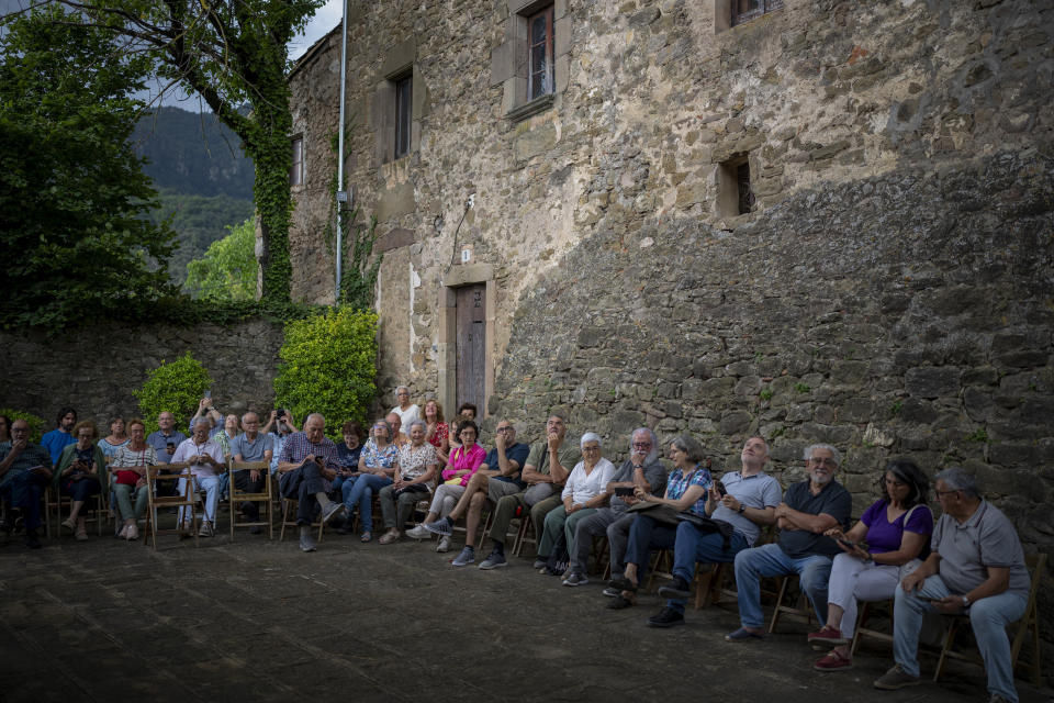 Local people sit around the12th-century Sant Romà church as they listen the students of the Vall d'en Bas School of Bell Ringers playing bells, in the tiny village of Joanetes about two hours north of Barcelona, Spain, Saturday, July 29, 2024. A school set up to revive the manual ringing of church bells has graduated its first class of 18 students after learning their ringing skills. (AP Photo/Emilio Morenatti)