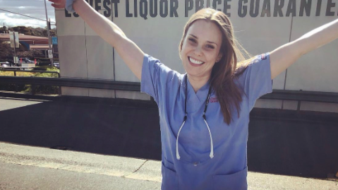 Georgia McDonald in scrubs with her arms in the air. 