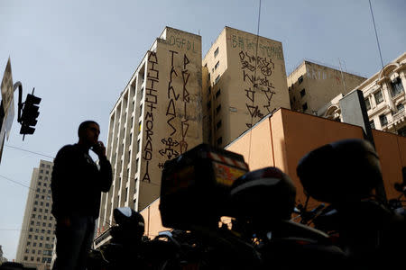 A man stands in front of a building tagged by "pichadores", graffiti artists who tag buildings and landmarks with angular, runic fonts, with their personal signatures, called "pichacao", on a street in Sao Paulo, Brazil, April 20, 2017. REUTERS/Nacho Doce