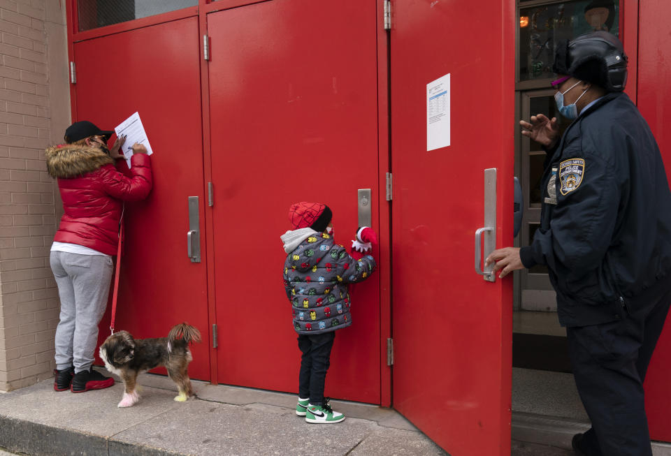 Sheila Melendez, left, completes a form granting permission for random COVID-19 testing for students as she arrives with her daughter Jayceon, center, at P.S. 134 Henrietta Szold Elementary School, Monday, Dec. 7, 2020, in New York. Public schools reopened for in-school learning Monday after being closed since mid-November. (AP Photo/Mark Lennihan)