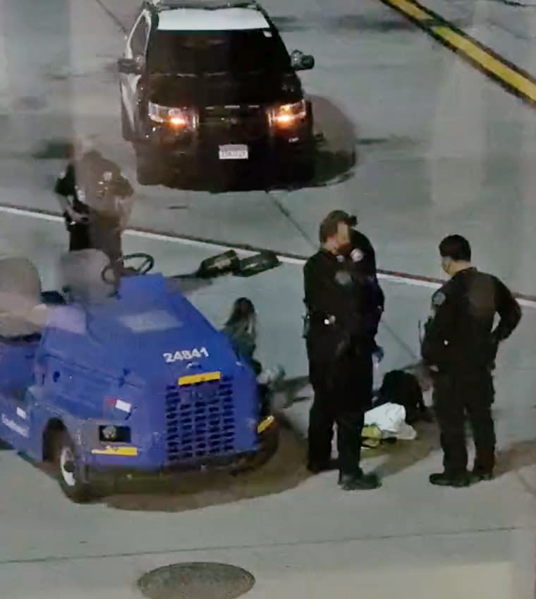 A woman who appears to have her hands cuffed behind her back sits on the tarmac after attempting to flag down a plane at Los Angeles International Airport. (@TezlynFigaro)