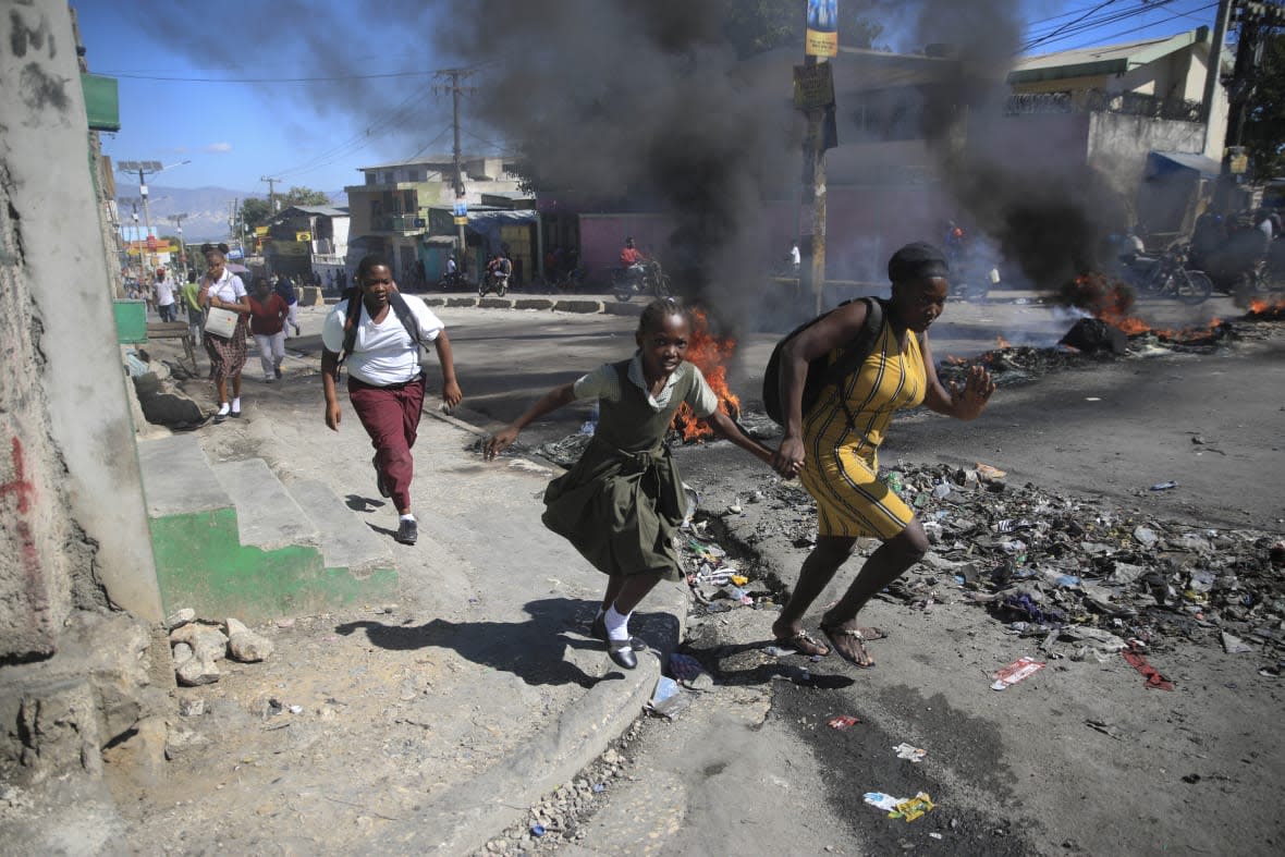 FILE – A woman and her daughter run past a barricade that was set up by police protesting bad police governance in Port-au-Prince, Haiti, Jan. 26, 2023. Haiti’s latest crisis entered full throttle following the 2021 assassination of President Jovenel Moïse, when current Prime Minister Ariel Henry emerged in a power struggle as the country’s leader and the country’s nearly 200 gangs have taken advantage of the chaos, warring for control. (AP Photo/Odelyn Joseph, File)