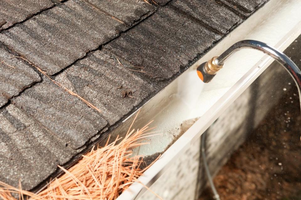 Using a power washer to clean leaves and debris out of rain gutters.