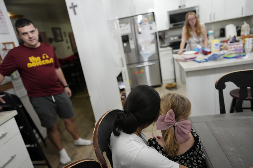 Sol, center left, a 14-year-old from Argentina, holds 8-year-old Maddie Hazelton on her lap as they hang out with Sol's foster parents, Andy, left, and Caroline Hazelton, in Homestead, Fla., Monday, Dec. 18, 2023. Sol is among tens of thousands of children who have arrived in the United States without a parent during a huge surge in immigrants that's prompting congressional debate to change asylum laws. (AP Photo/Rebecca Blackwell)