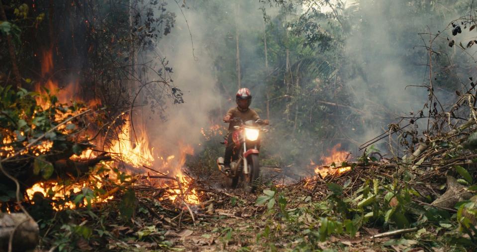 An invader rides his motorcycle through the rainforest fire blaze.<span class="copyright">Alex Pritz—Amazon Land Documentary</span>