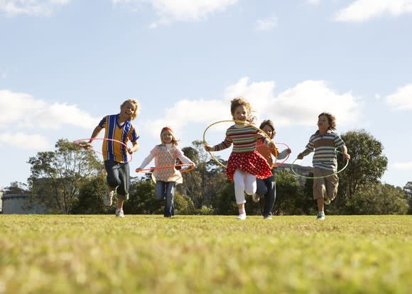 Five children with Hula Hoops running in a grass field on a sunny day.