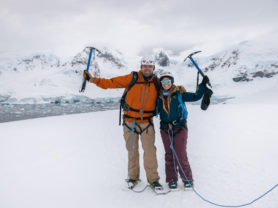 A couple standing in a snowy environment with tools in their hand.