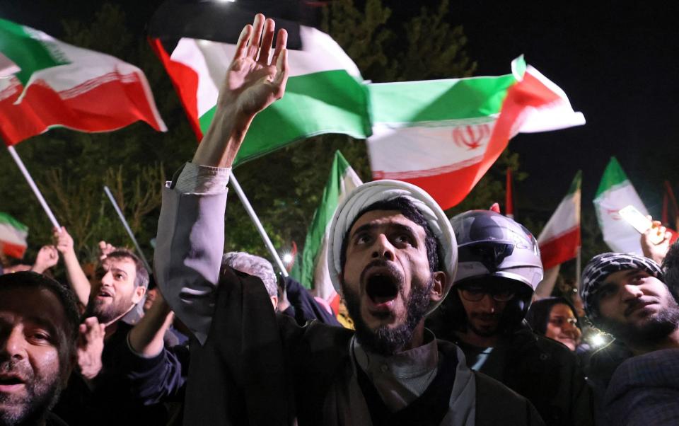 Demonstrators wave Iran's flag and Palestinian flags as they gather in front of the British Embassy in Tehran