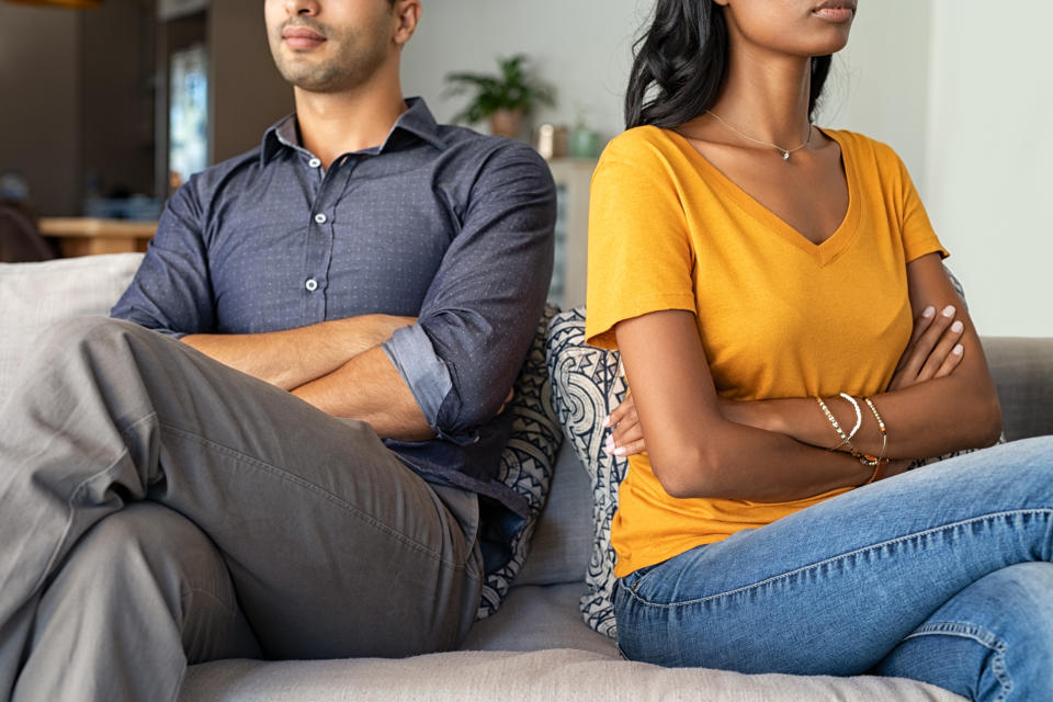 A man and woman sit on a couch with arms crossed, facing away from each other, suggesting a disagreement or conflict. Names unknown