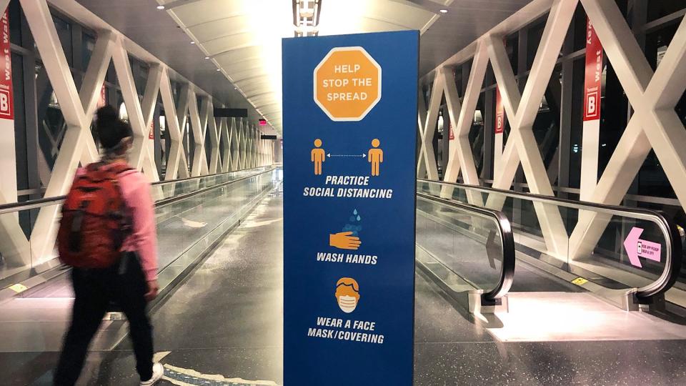 A woman walks past a sign encouraging travelers to help stop the spread of coronavirus, practice social distancing, wash hands, and wear a face mask or covering, at Boston Logan International Airport