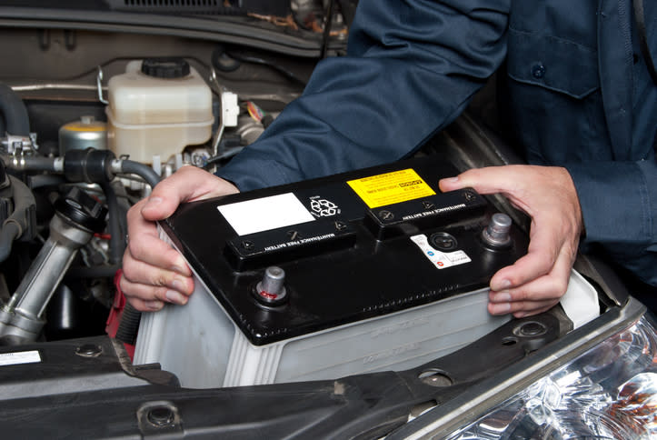 Technician installing a car battery under the vehicle's hood