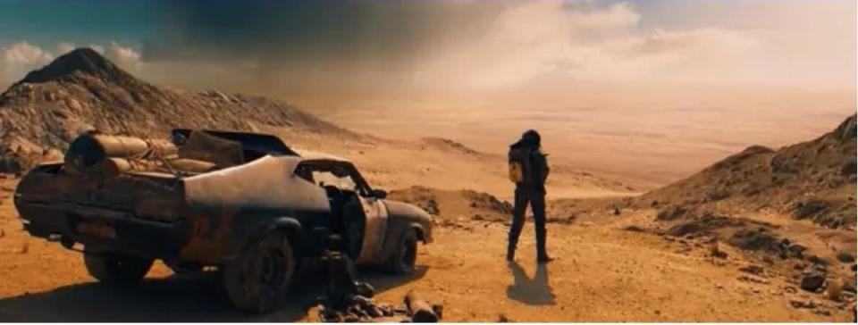 A person standing in front of a burned-out car and looking out over a barren landscape