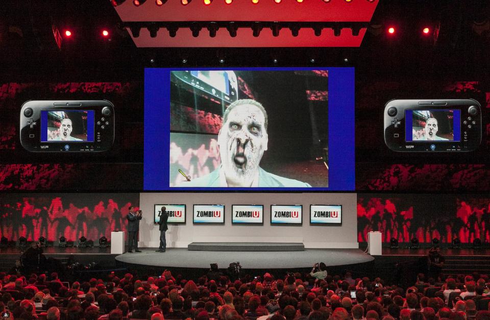 Reggie Fils-Aime, president and CEO of Nintendo America, Inc., center, is digitally transformed into a zombie, as he plays Ubisoft's new title "ZombiU," an exclusive Wii U zombie game released at the Nintendo All-Access presentation at E3 2012 in Los Angeles Tuesday, June 5, 2012. The Electronic Entertainment Expo runs from June 5-7 at the Los Angeles Convention Center. (AP Photo/Damian Dovarganes)