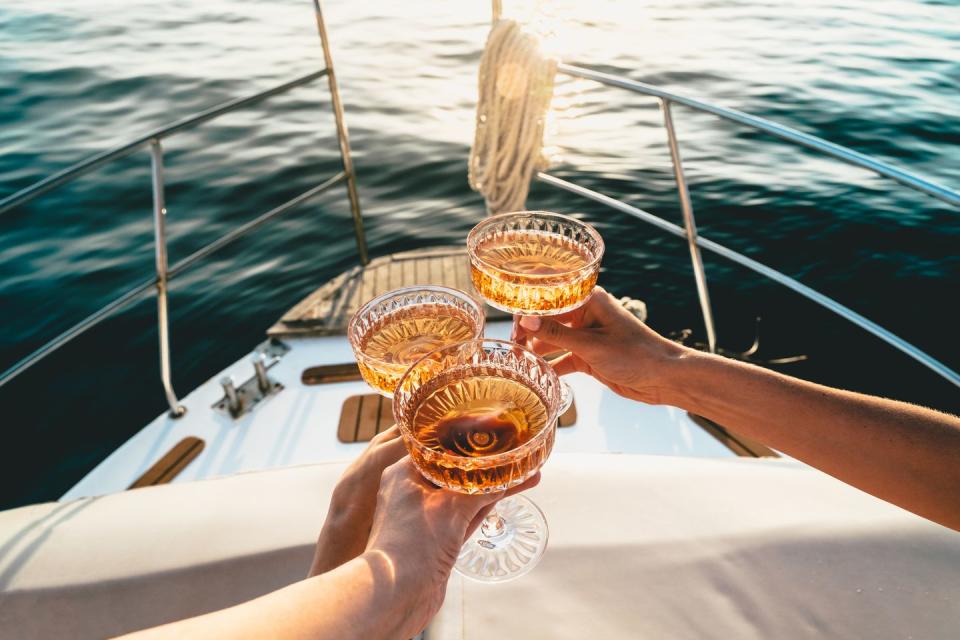 friends clinking sparkling wine glasses at sunset on a yacht
