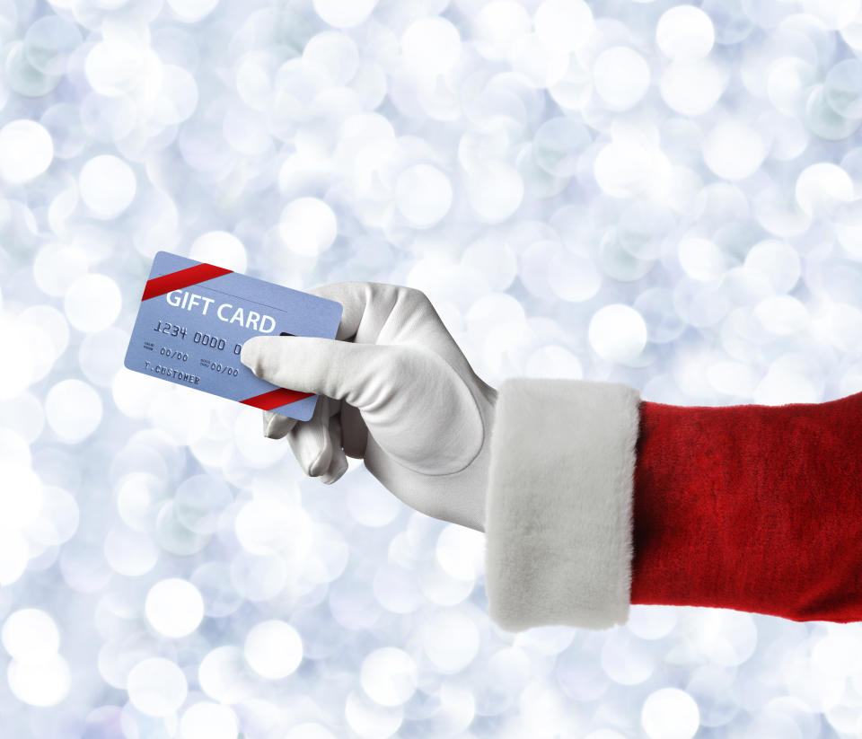 A close up of Santa Claus holding a gift card in front of a field of blurred Chhristmas lights.