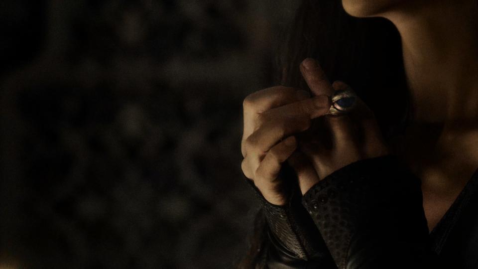 A close-up on Moiraine, focusing on the middle finger of her left hand as she dons her Aes Sedai ring, an oversized golden ring with a large blue gemstone with a serpent eating its own tail surrounding it