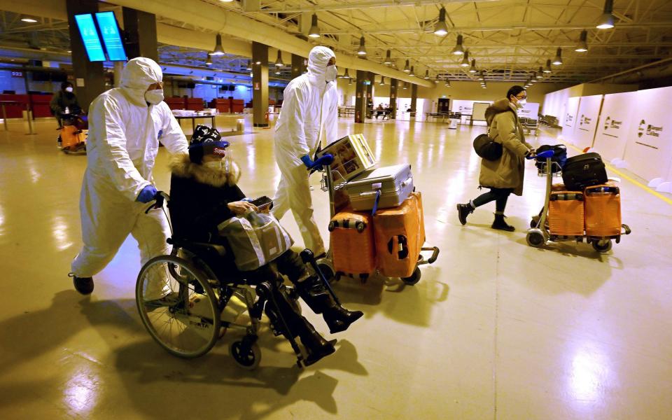 Workers wearing protective masks and suits help Chinese travellers leaving the arrival hall of Rome Fiumicino International Airport