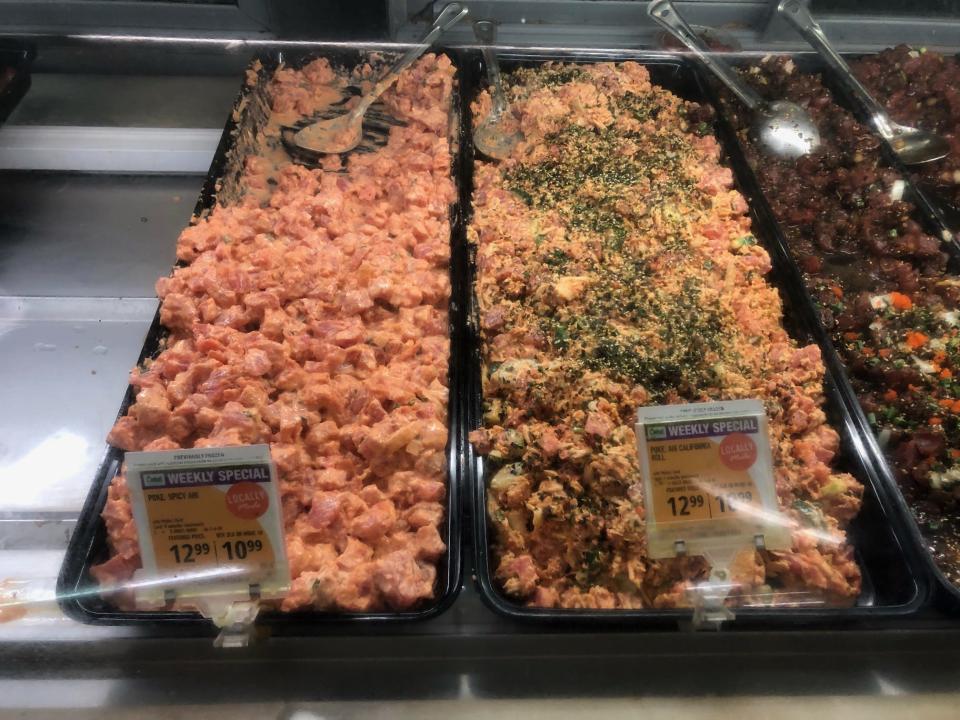 Two trays of poke at Sack N Save, one of spicy ahi poke and a "California roll" variety with imitation crab meat, cucumbers, and furikake mixed in.
