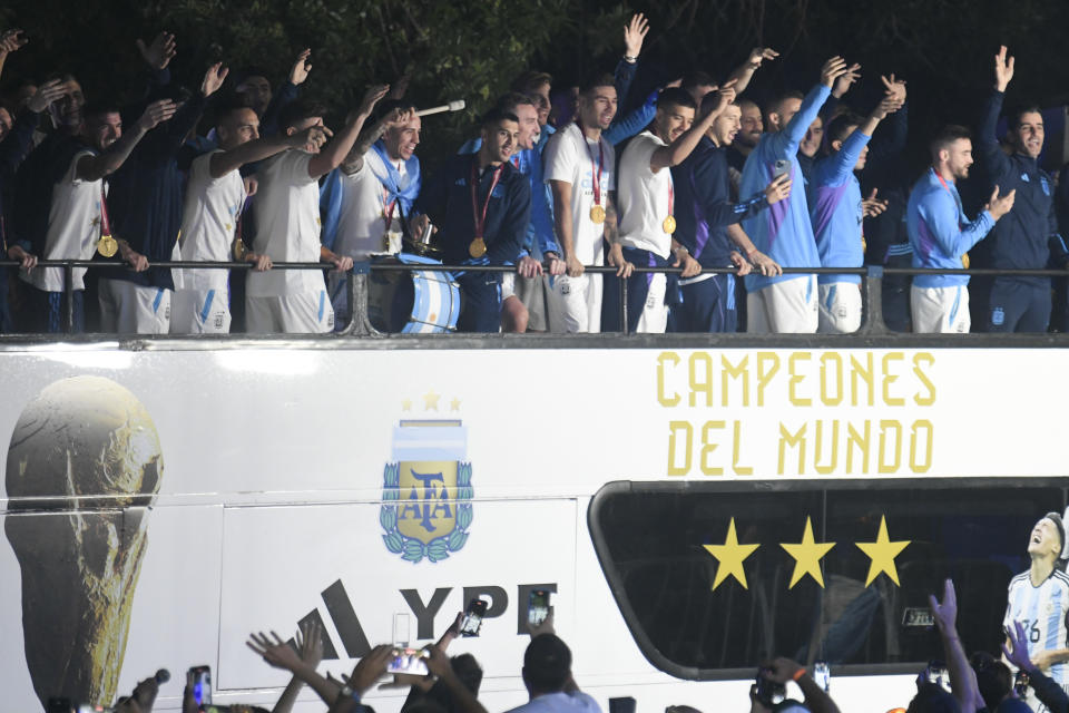 Miembros de la selección argentina de fútbol saludan desde el bus que les lleva a la sede de la Asociación del Fútbol Argentino, donde pasarían la noche tras aterrizar en el aeropuerto de Ezeiza, a las afueras de Buenos Aires, Argentina, el martes 20 de diciembre de 2022. (AP Foto/Gustavo Garello)