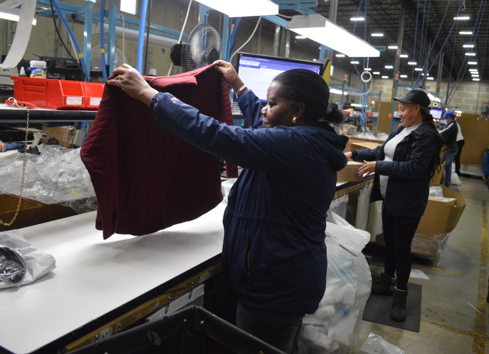 A women in a drk top holds up a red short to inspect in at a brightly-lit workstation inside a warehouse.