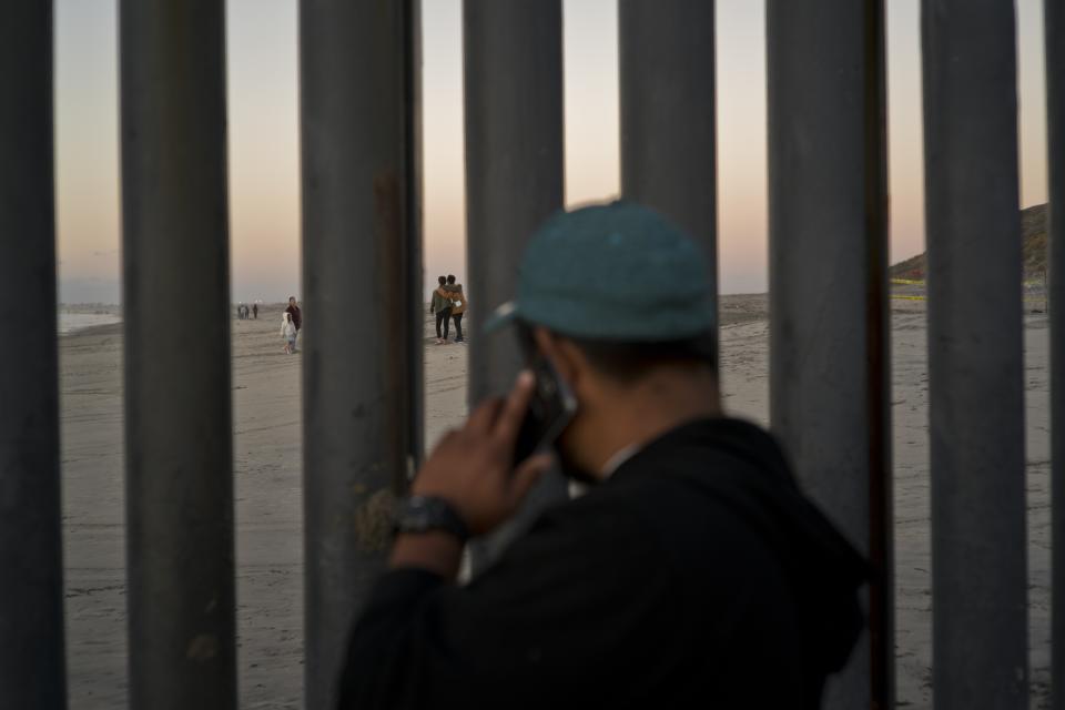 A man talks on his mobile phone as he looks across the border structure, in Tijuana, Mexico, Friday, Nov. 23, 2018. The mayor of Tijuana has declared a humanitarian crisis in his border city and says that he has asked the United Nations for aid to deal with the approximately 5,000 Central American migrants who have arrived in the city. (AP Photo/Ramon Espinosa)