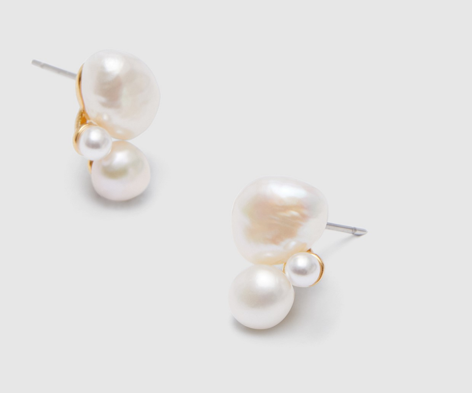 Two stacked pearl stud earrings on pale grey background.