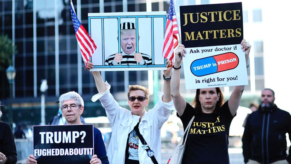 Protestors hold banners before the arrival of former President Donald Trump to New York State Supreme court for the start of the civil fraud trial against him on October 2, 2023 in New York City. Donald Trump faces fresh legal danger as a civil fraud trial against the former president and two of his sons begins in New York, threatening the Republican frontrunner's business empire as he campaigns to retake the White House with four criminal cases looming.