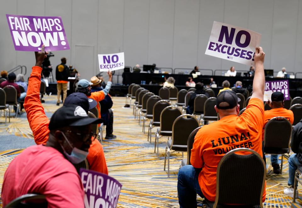 Members of the metro Detroit community hold signs that say "Fair Maps Now" and "No Excuses" as The Michigan Independent Citizens Redistricting Commission holds its first public hearing on Oct. 20, 2021, at the TCF Center in Detroit. The hearings are an effort to solicit input on the draft maps they've drawn.