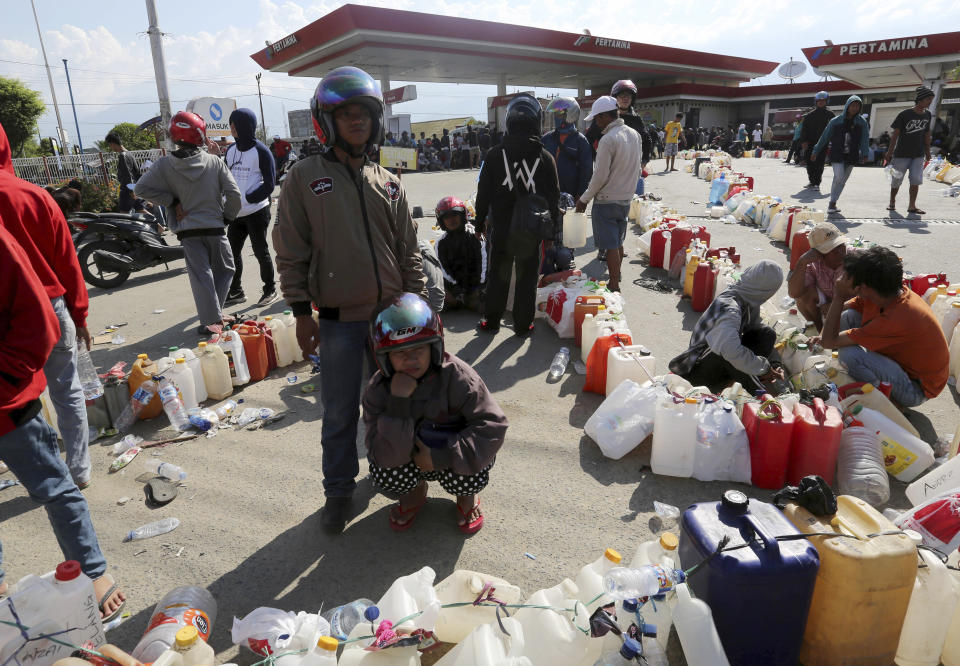 People queue for gasoline following a massive earthquake and tsunami at a gas station in Palu, Central Sulawesi, Indonesia, Monday, Oct. 1, 2018. A mass burial of earthquake and tsunami victims was being prepared in a hard-hit city Monday as the need for heavy equipment to dig for survivors of the disaster that struck a central Indonesian island three days ago grows desperate. (AP Photo/Tatan Syuflana)